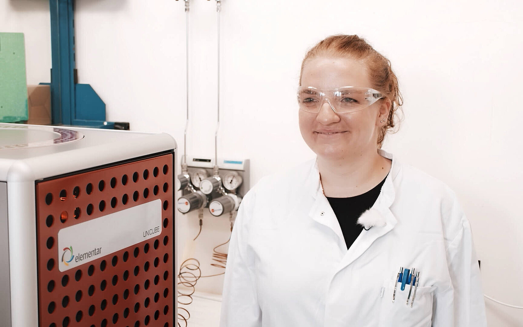 A lab technician stands beside an elemental analyzer for net peptide content analysis